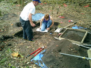 Two archaeologists excavating a pit to study the area near an old plantation wall