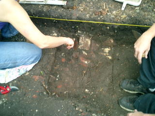 Two archaeologists clearing soil away from an old brick foundation or fallen wall